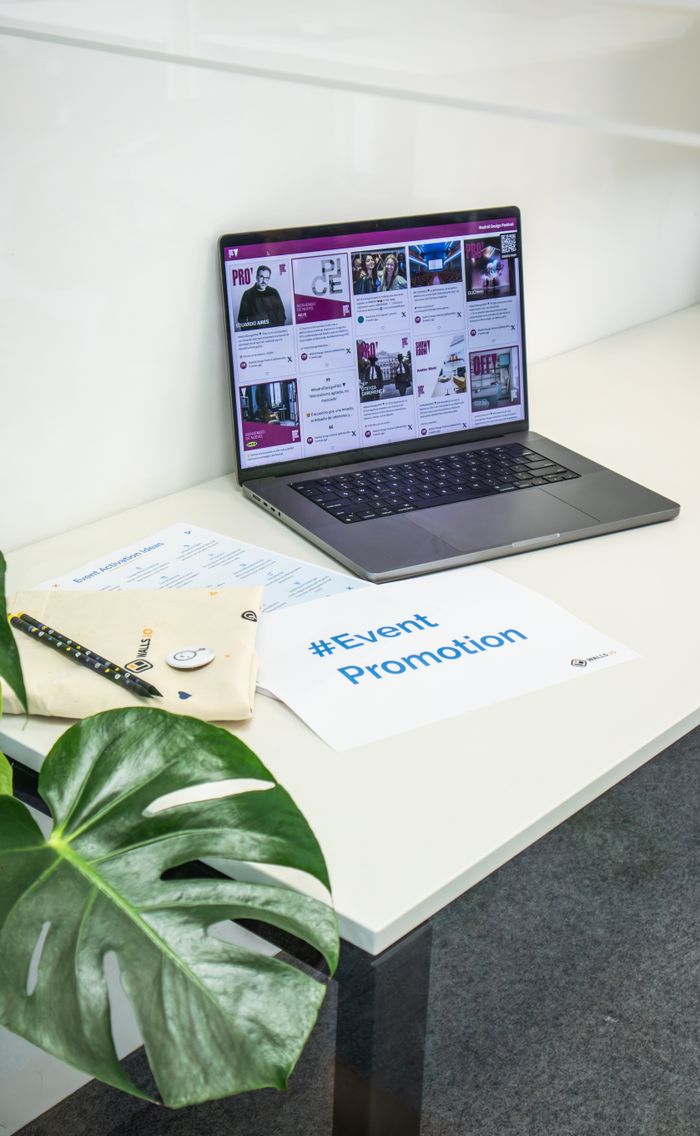 Un espace de bureau épuré avec un ordinateur portable affichant les réseaux sociaux, des documents et une plante pour la promotion d’un événement.